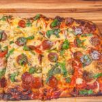 Immagine di una pizza in teglia con lievitazione non riuscita, evidenziando la crosta bassa e compatta.