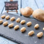 Gnocchi di patate appena preparati su un piano di lavoro con ingredienti e strumenti per la ricetta.