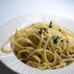 Pasta al limone con crema vellutata, decorata con scorza di limone e foglie di basilico.