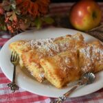 Frittelle di mele al forno dorate, servite su un piatto con zucchero a velo e cannella.