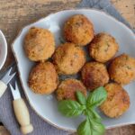 Arancini dorati e croccanti su un piatto, pronti per essere fritti senza aprirsi.
