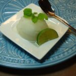 Sorbetto al limone servito in una coppa, decorato con fettine di limone e menta fresca.